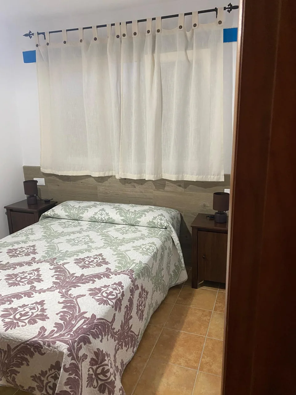 Segundo dormitorio con cama de matrimonio, colcha estampada y cortinas blancas