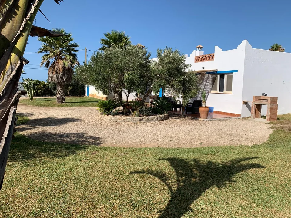 Fachada blanca de Casa Poniente con detalles azules y palmeras en el jardín