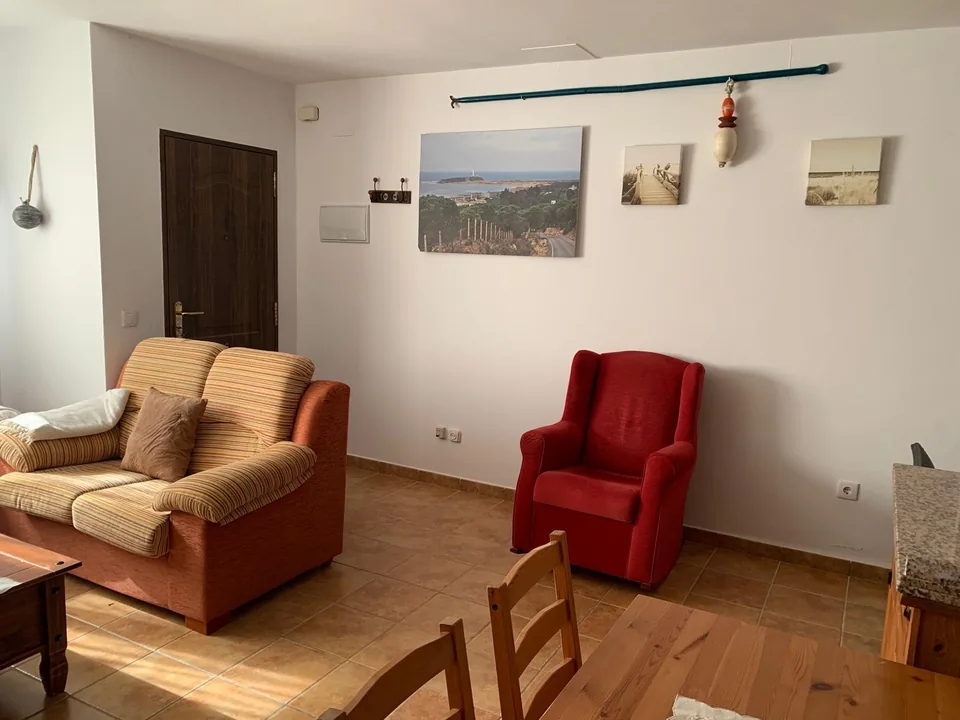 Rincón del salón con sillón rojo y sofá junto a la pared decorada